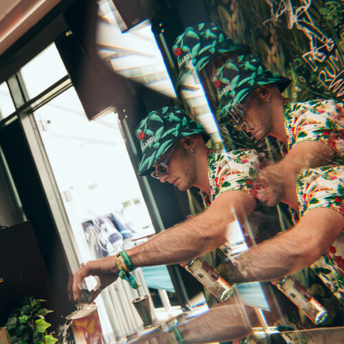 Two bartenders in green patterned hats pouring drinks